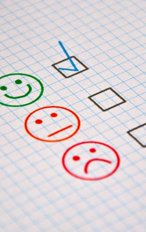Three tickboxes next to green smiling, orange neutral, and red sad faces are drawn on graph paper. The tickbox next to the green smiling face is ticked, indicating a positive response.