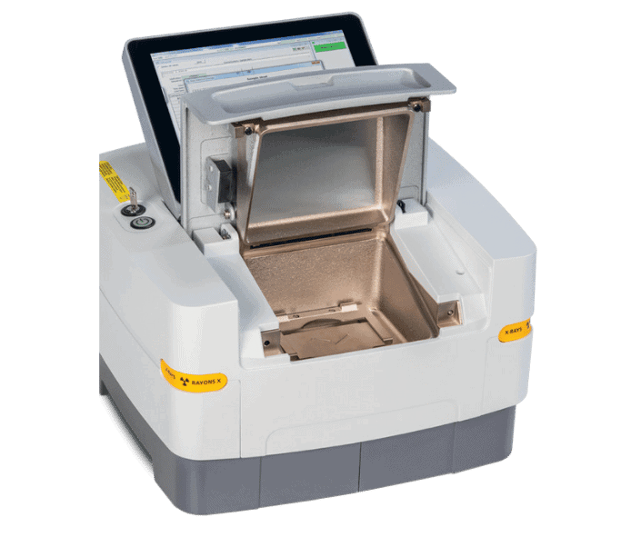 A laboratory X-ray fluorescence (XRF) analyser with its sample chamber open, showing the metal interior and touchscreen display, used for material and element analysis.